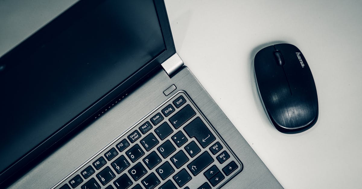Close-up of a silver laptop and black wireless mouse on a white desk.